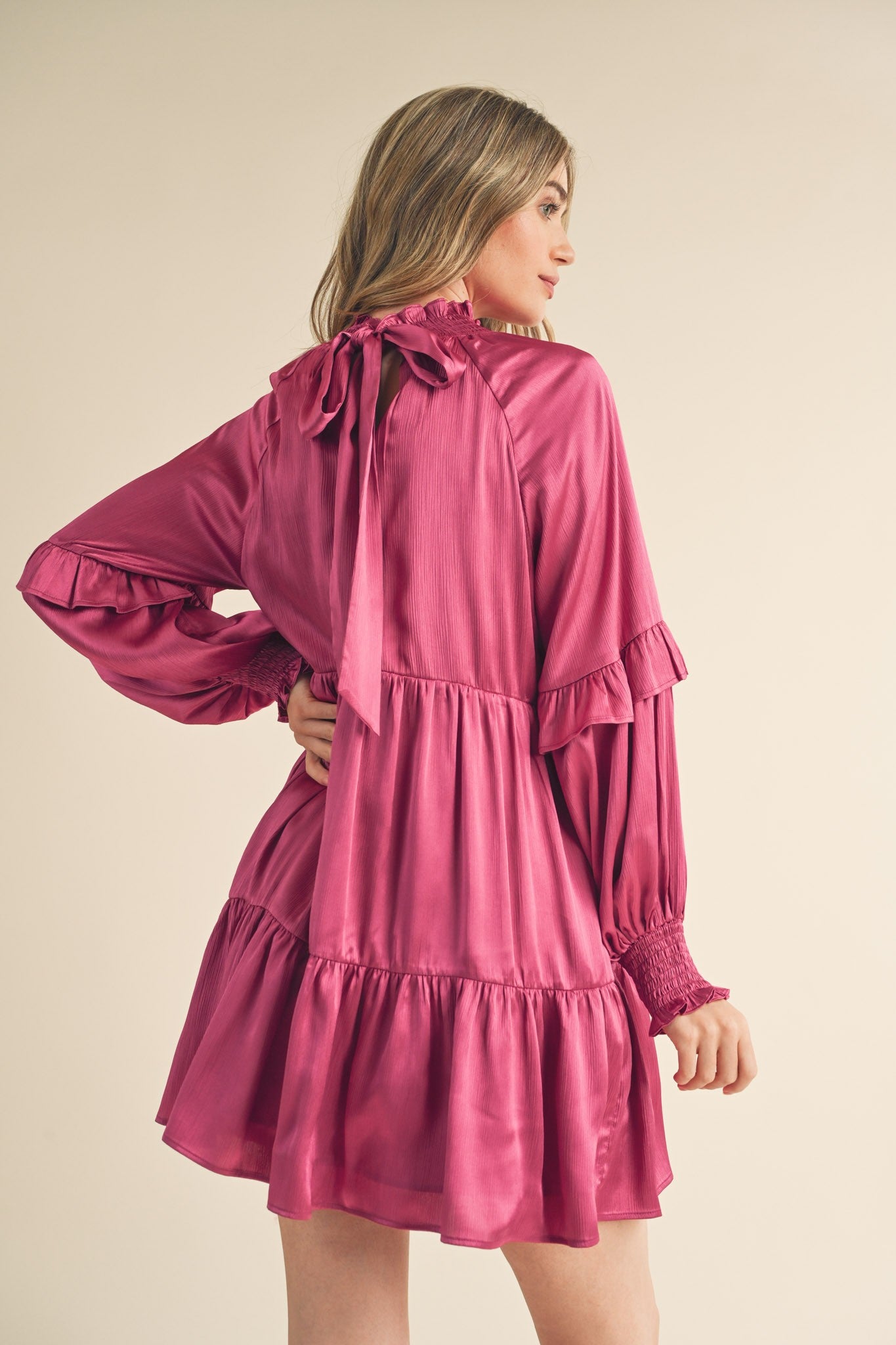 woman wearing a magenta ruffled mini dress with a tie at the neck and long sleeves