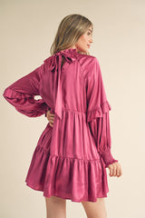 woman wearing a magenta ruffled mini dress with a tie at the neck and long sleeves