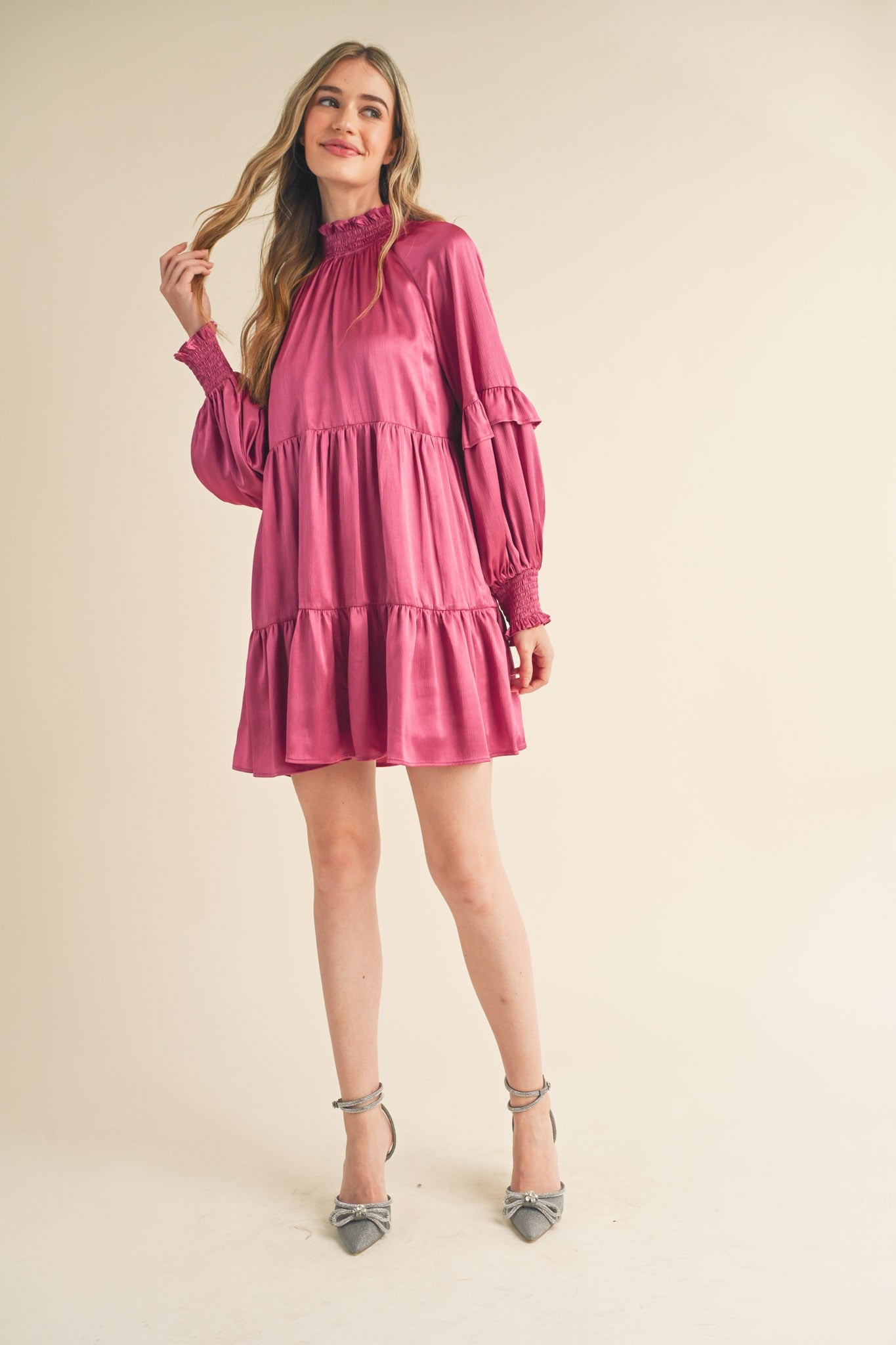 woman wearing a pink tiered mini dress with ruffle details and long sleeves, styled with gray heels