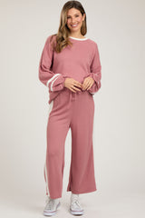 woman wearing a pink maternity sweater and matching wide-leg pants, holding her baby bump