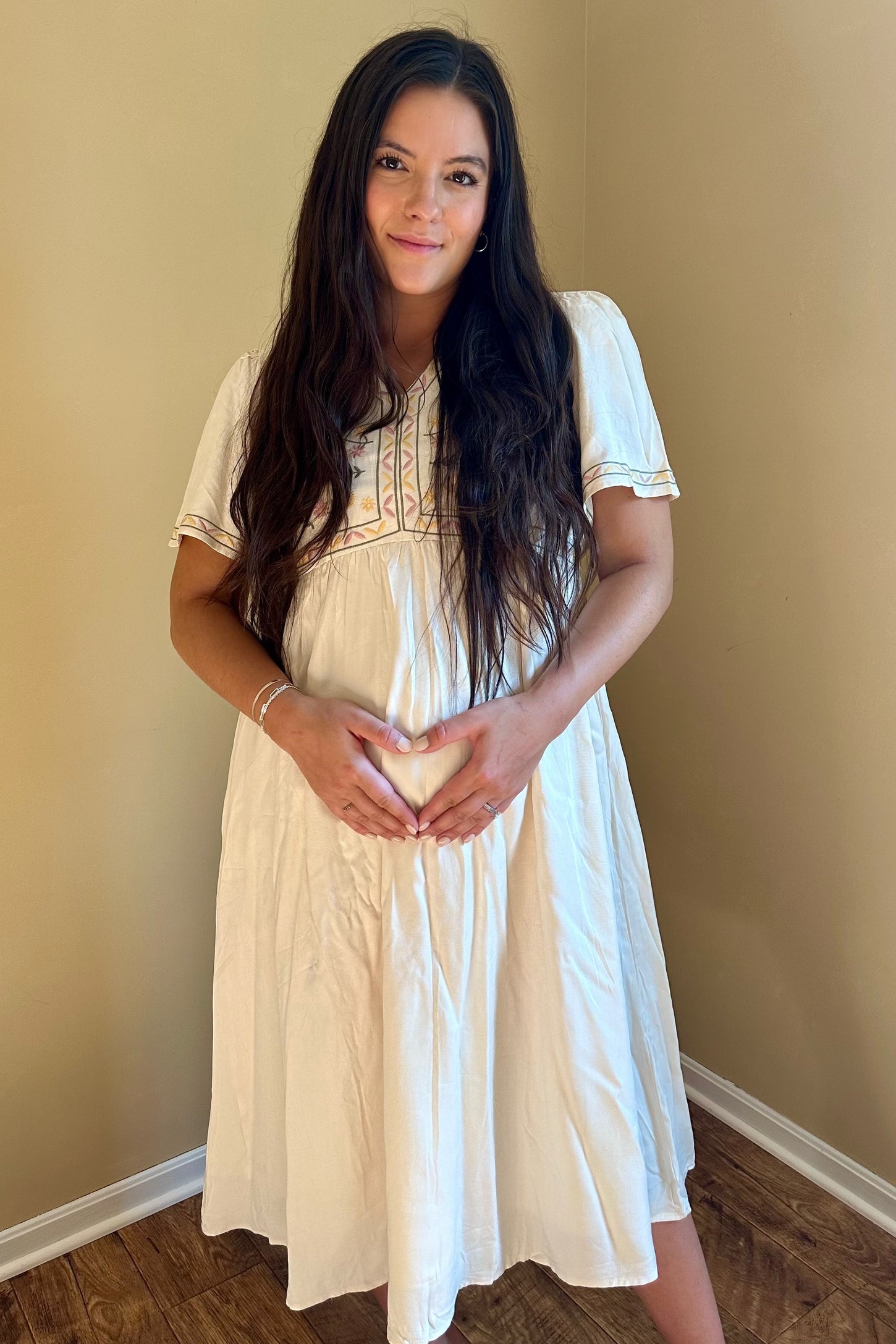 woman wearing a white embroidered maternity dress and holding her baby bump