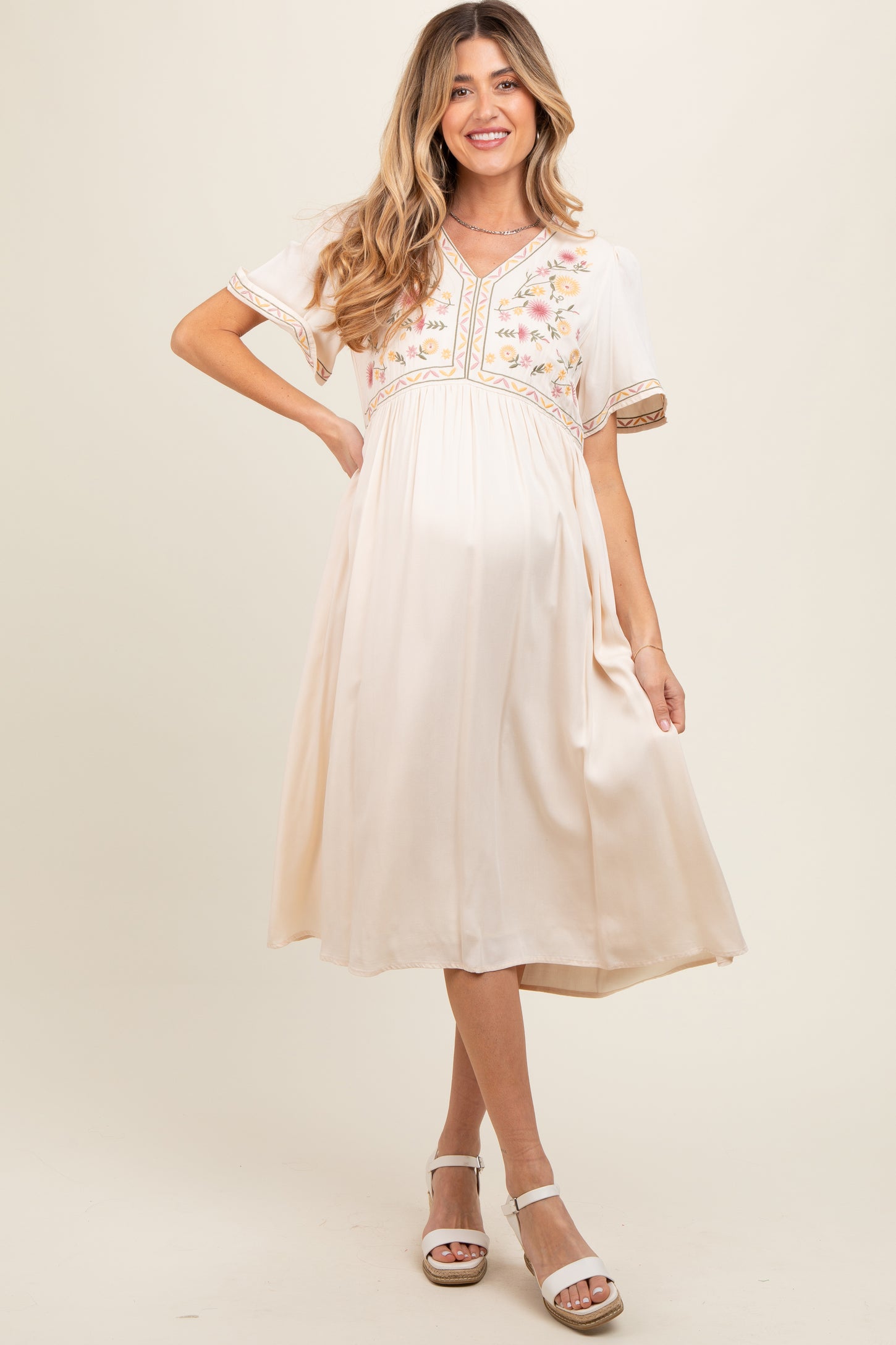 woman wearing a cream maternity dress with floral embroidery and short sleeves, baby bump visible