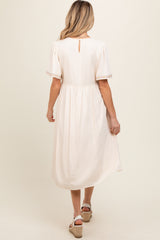 woman wearing a light pink maternity dress with short sleeves and a back keyhole detail