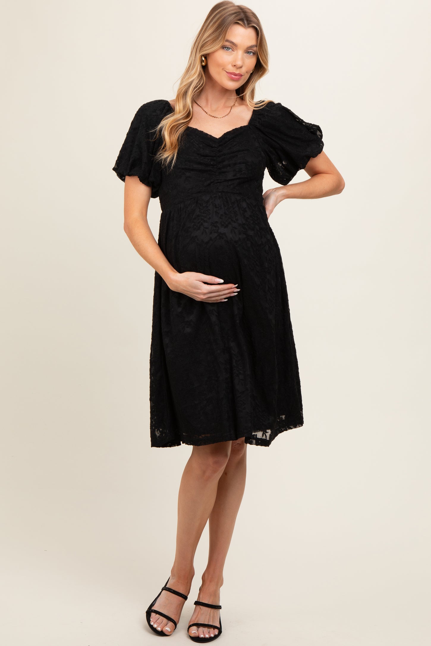woman wearing a black lace maternity dress with short puff sleeves and a baby bump visible