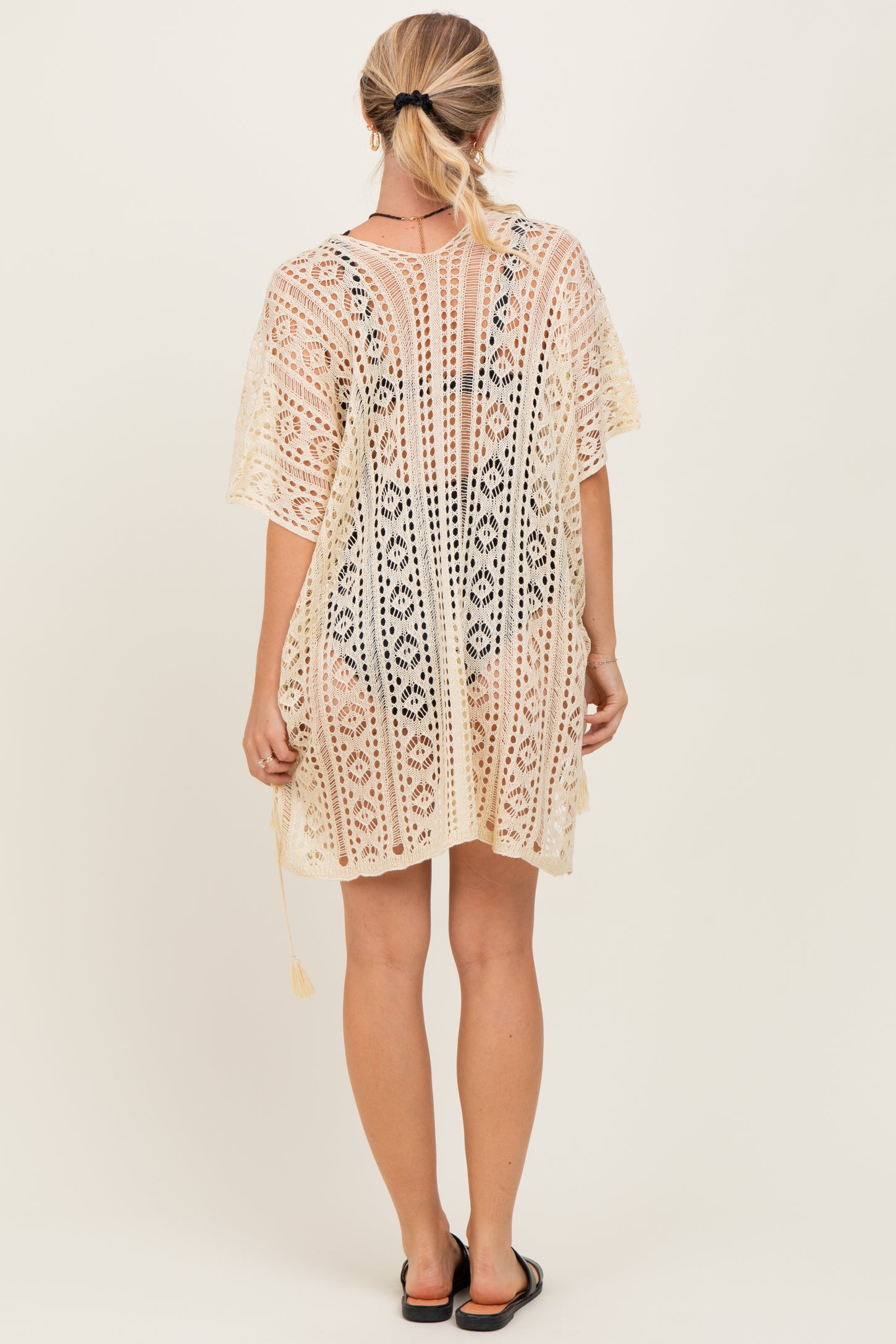 woman wearing a beige crochet cover-up with intricate patterns and short sleeves, shown from the back