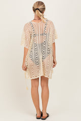 woman wearing a beige crochet cover-up with intricate patterns and short sleeves, shown from the back