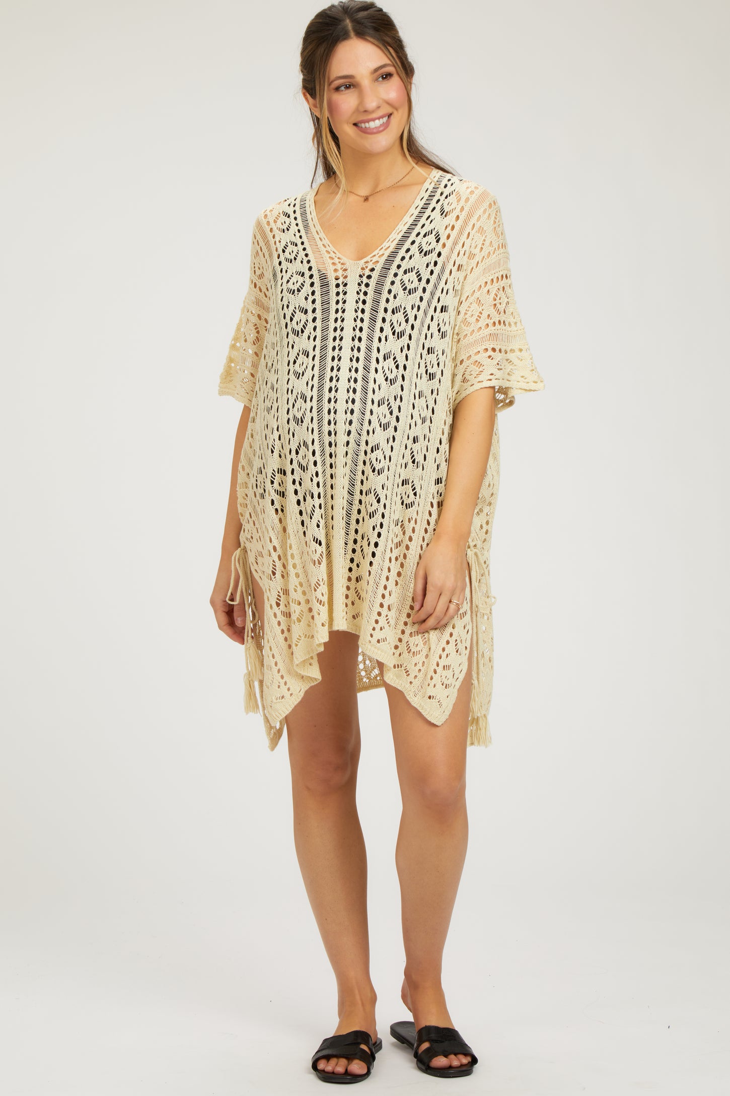 woman wearing a cream crochet maternity cover-up with a v-neck and side ties, showcasing her baby bump