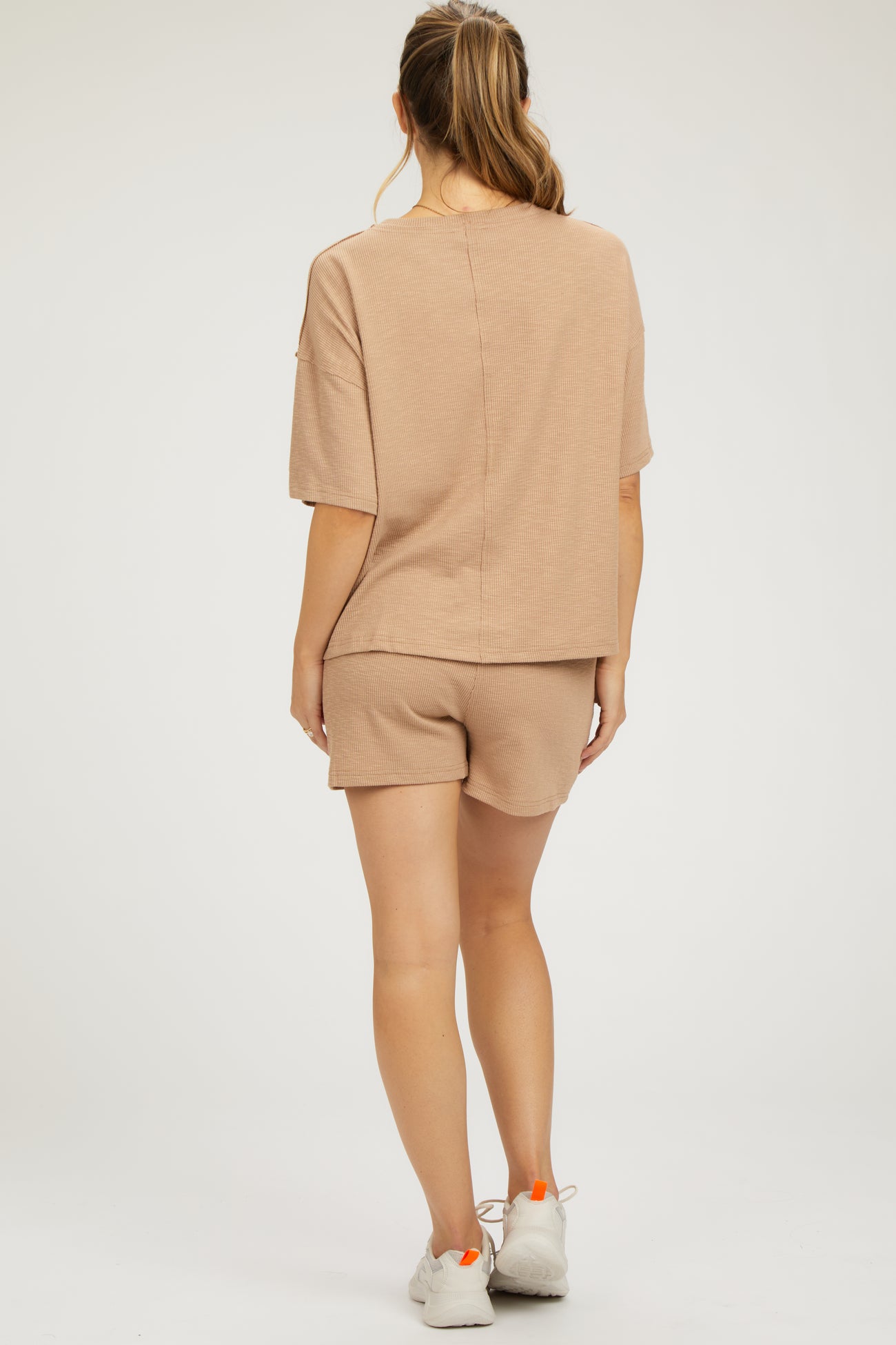 woman wearing a beige maternity loungewear set with a short sleeve top and shorts, showing a comfortable back view