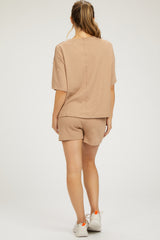 woman wearing a beige maternity loungewear set with a short sleeve top and shorts, showing a comfortable back view