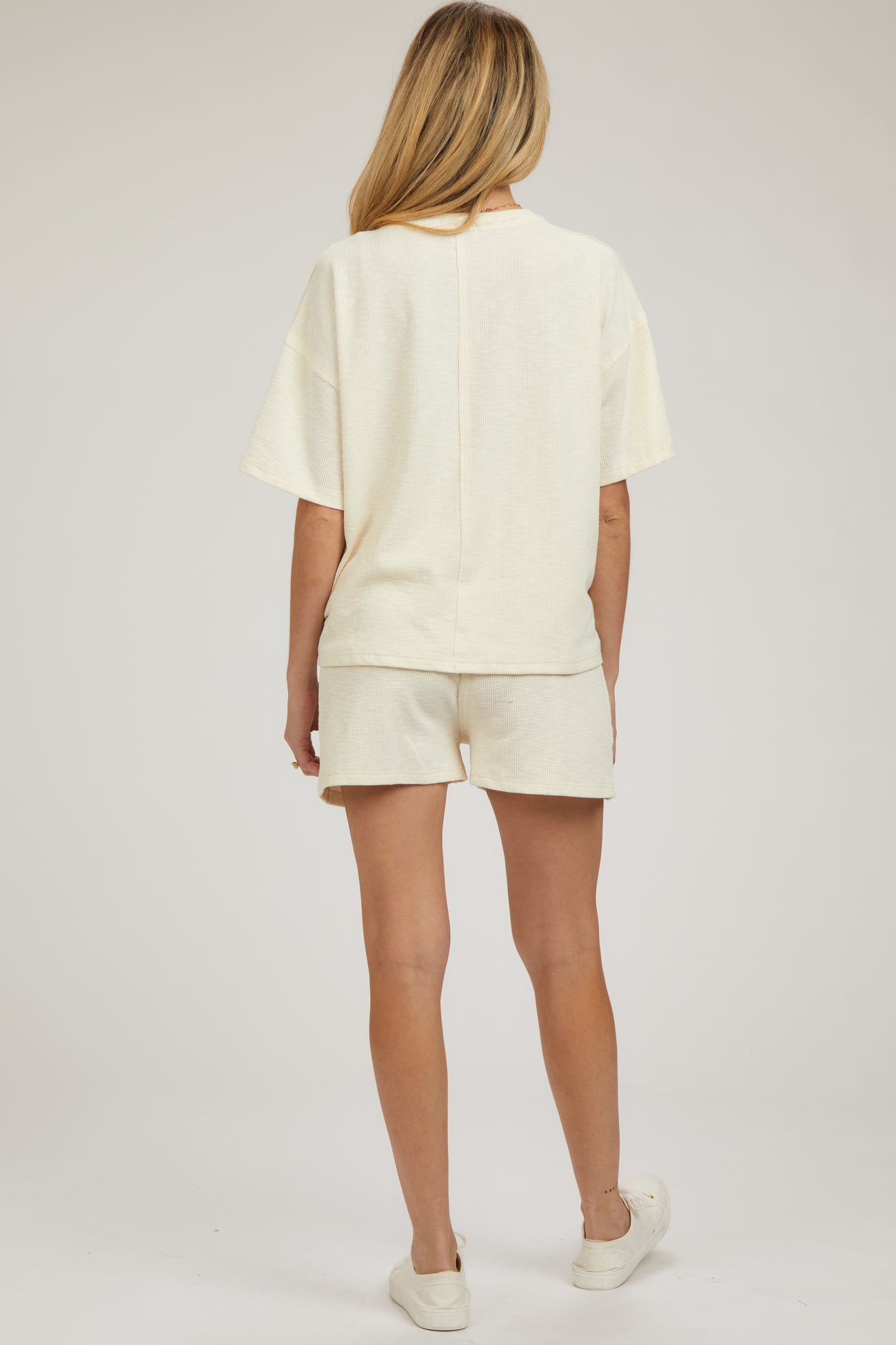 woman wearing a light cream maternity loungewear set, consisting of a short-sleeve top and shorts, with a relaxed fit