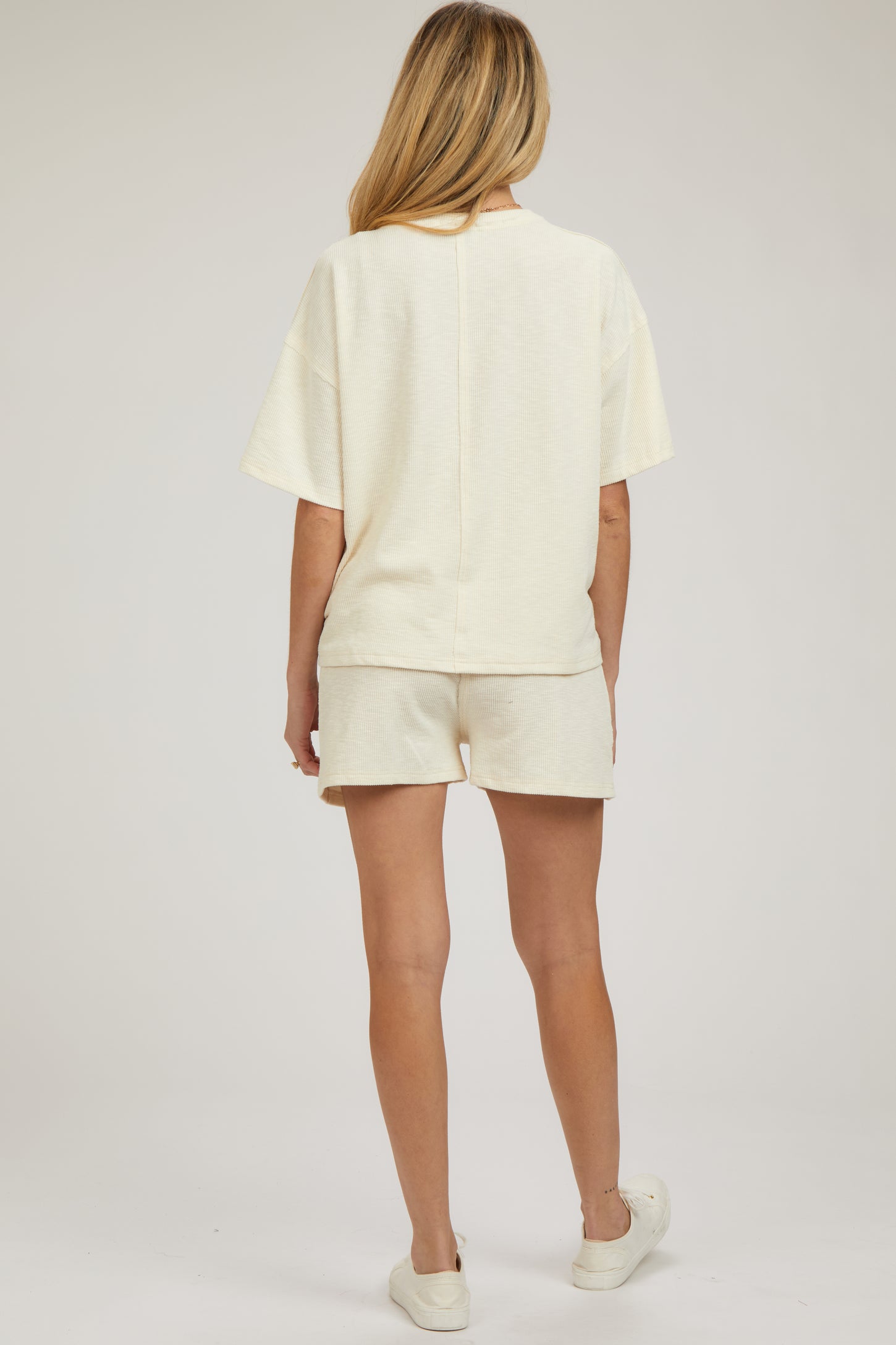 woman wearing a light cream maternity loungewear set, consisting of a short-sleeve top and shorts, with a relaxed fit