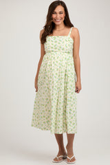 woman wearing a light green floral maternity dress with a fitted bodice and flowing skirt, showcasing a baby bump