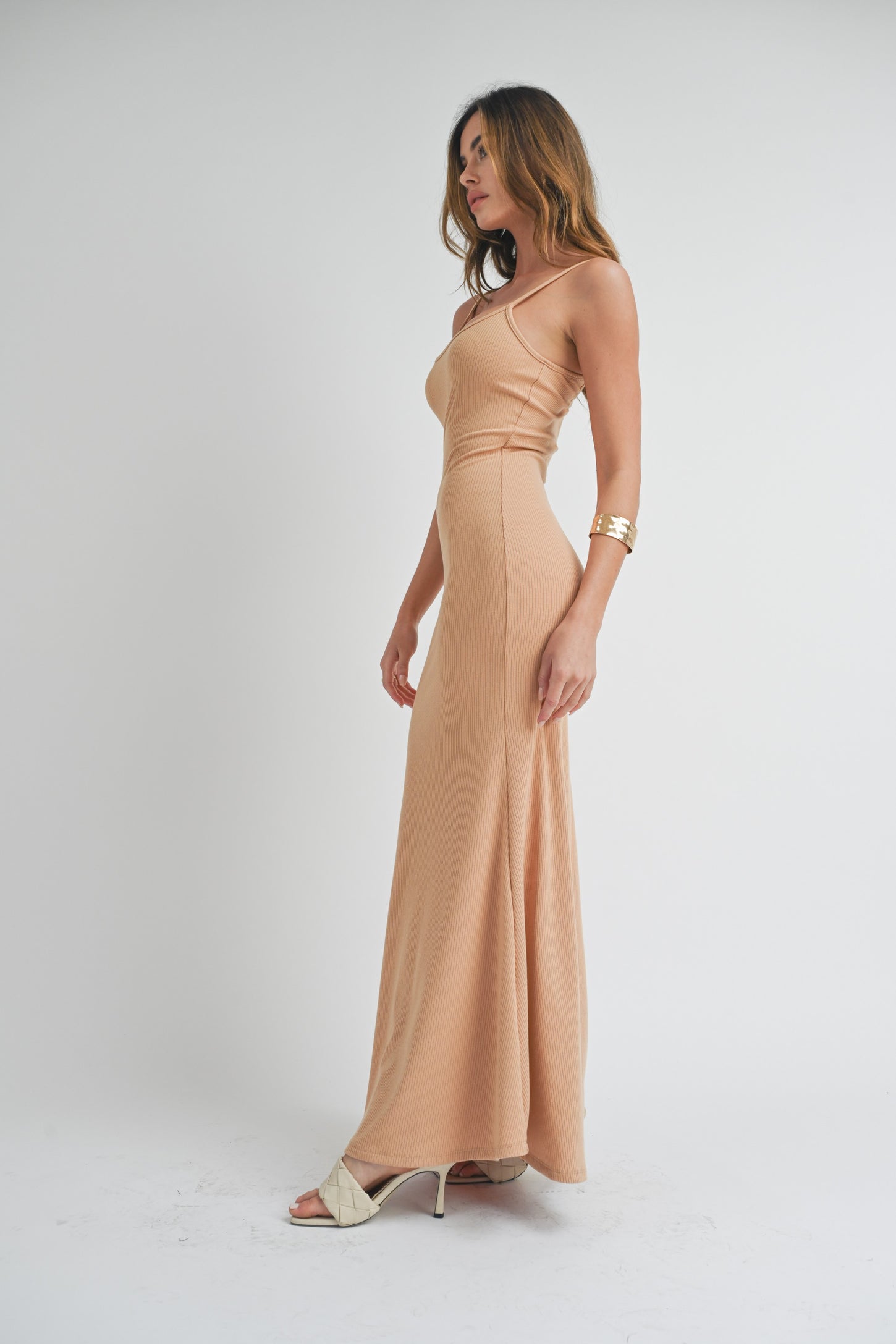 woman wearing a nude fitted maxi dress with ribbed texture and a side slit, standing in profile against a neutral background
