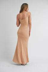 woman wearing a form-fitting beige spaghetti strap maxi dress, shown from the back