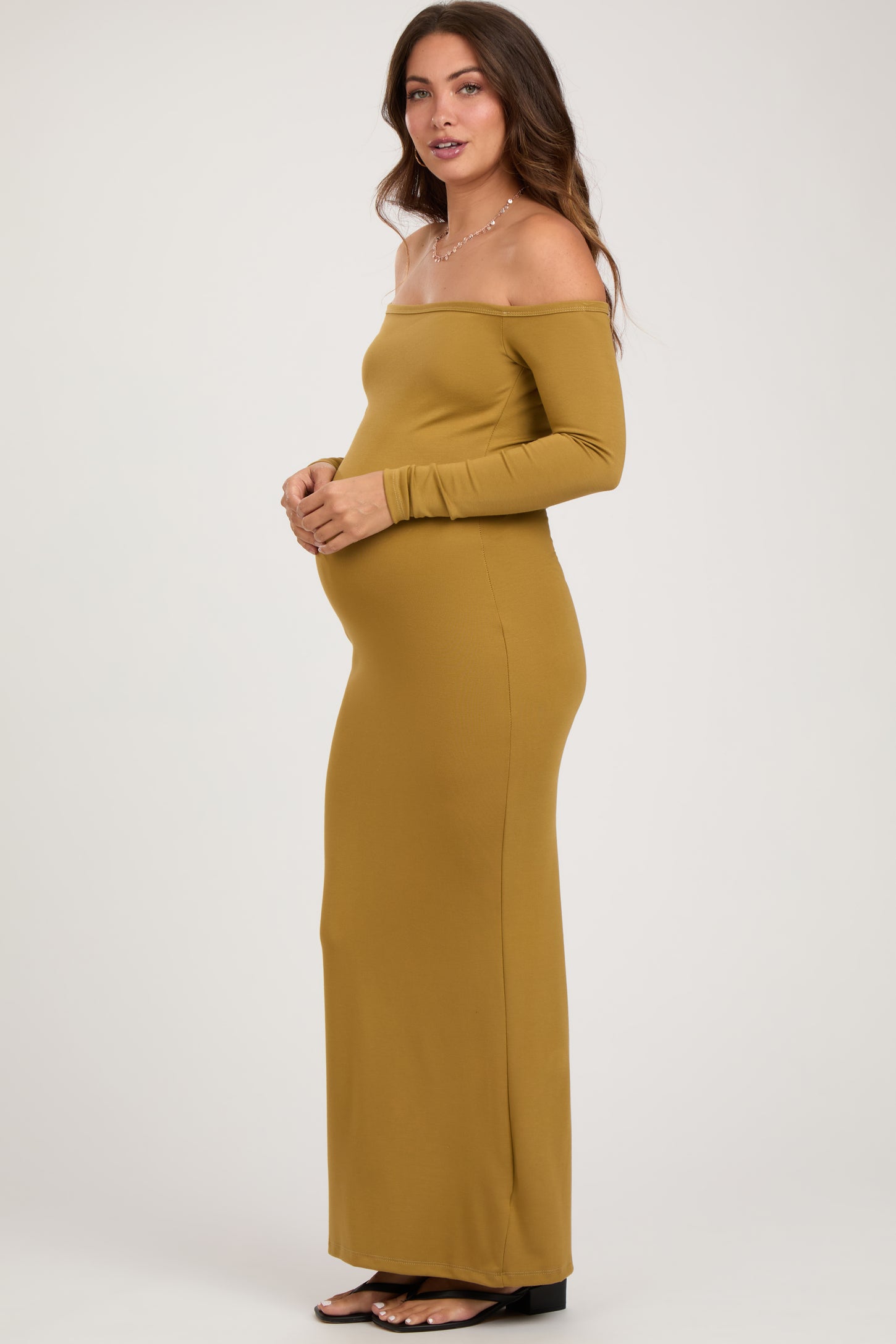 woman wearing a mustard off-shoulder maternity gown, showcasing her baby bump