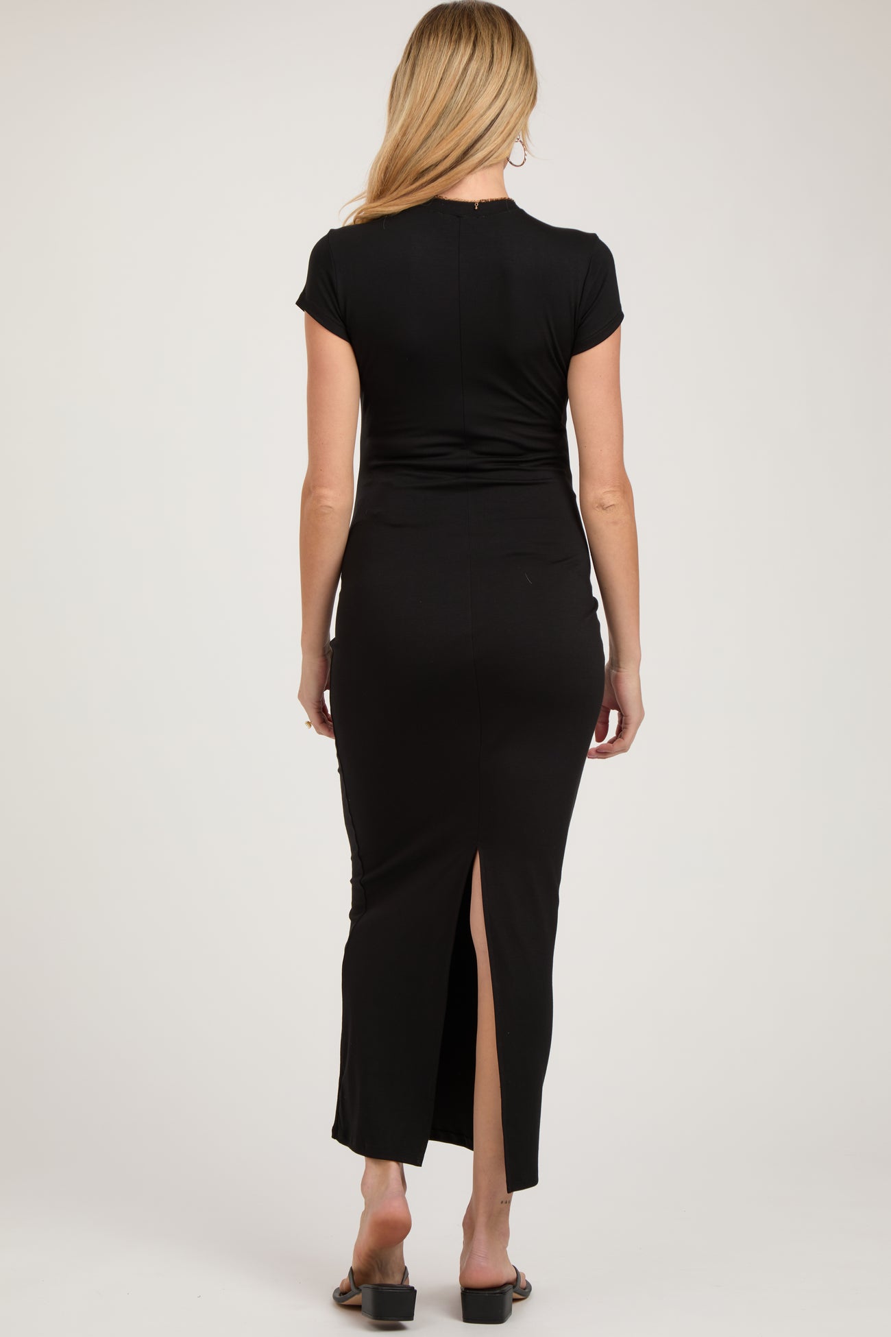 woman wearing a black maternity maxi dress with a back slit, showing her pregnant belly from the back