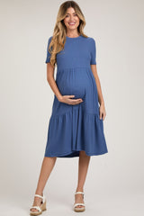 woman wearing a blue short sleeve maternity dress with a tiered hem and holding her baby bump