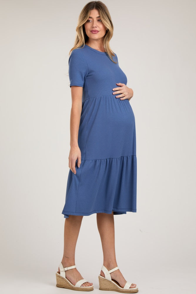 woman wearing a blue short sleeve maternity dress with a tiered skirt and holding her baby bump