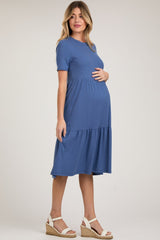 woman wearing a blue short sleeve maternity dress with a tiered skirt and holding her baby bump