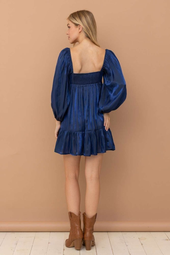 woman wearing a navy blue puff sleeve mini dress with a smocked bodice and ruffled hem, styled with brown ankle boots