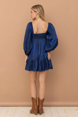 woman wearing a navy blue puff sleeve mini dress with a smocked bodice and ruffled hem, styled with brown ankle boots