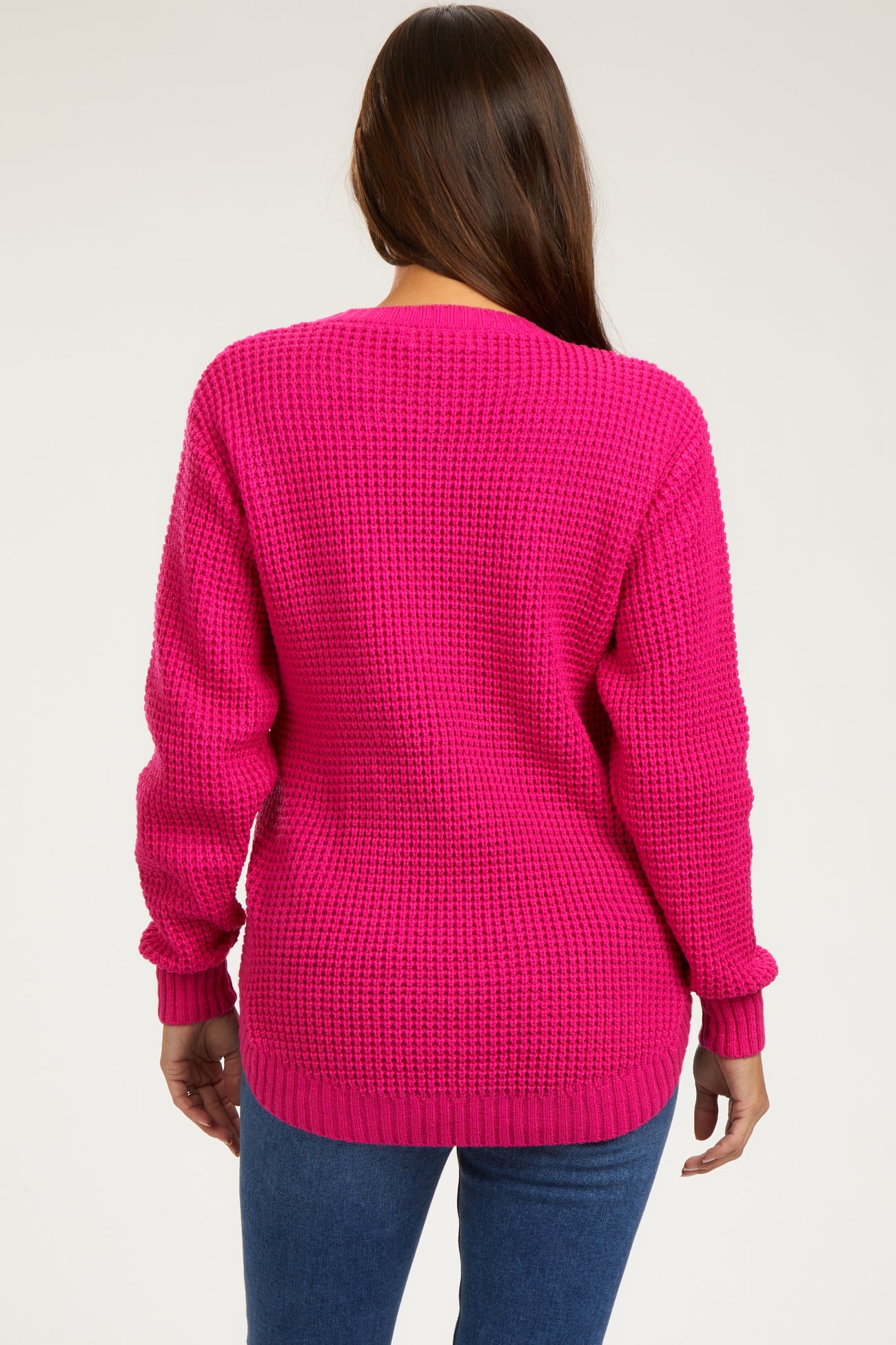 woman wearing a bright pink knitted maternity sweater, showing a relaxed fit and long sleeves from the back