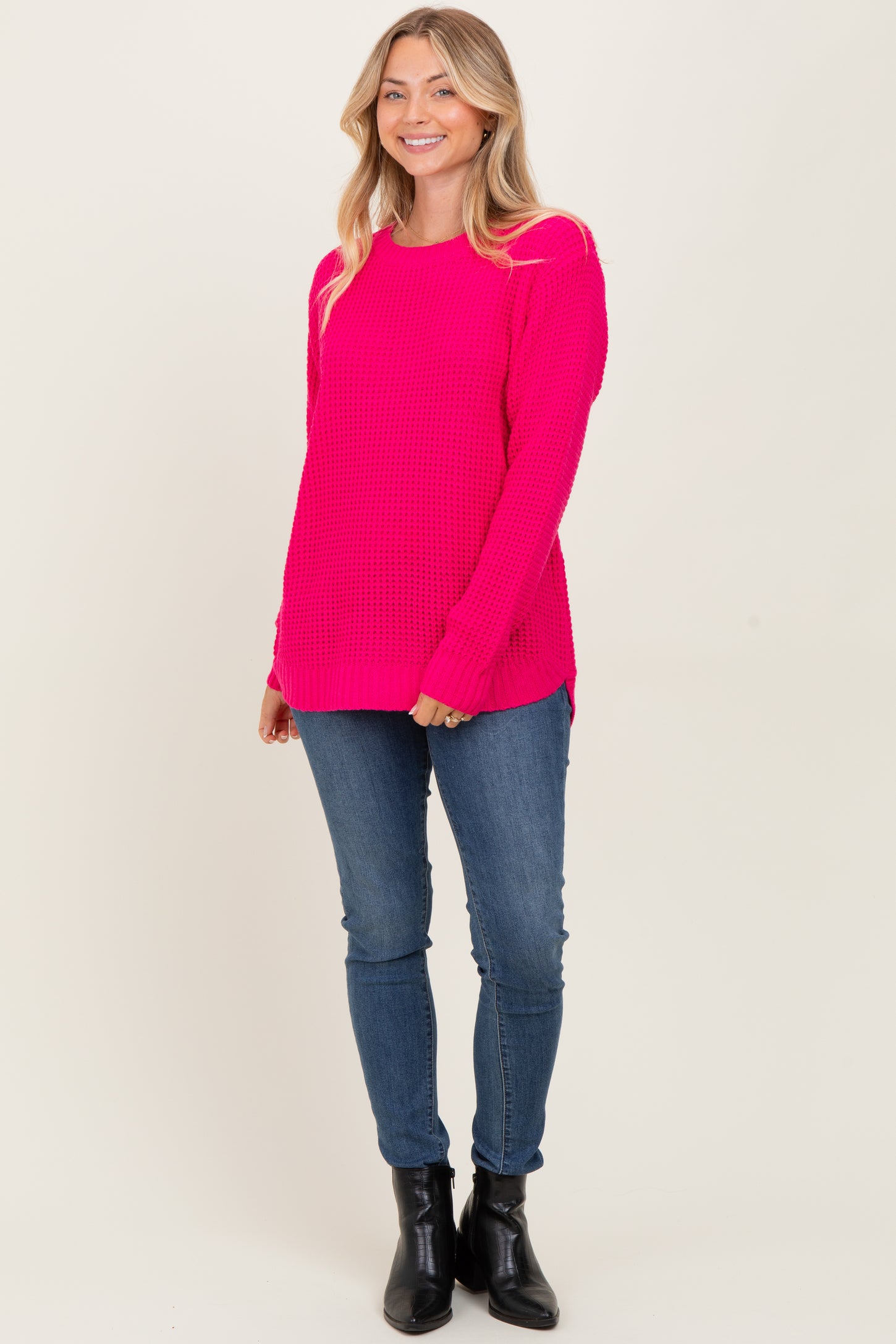 woman wearing a bright pink knit sweater with long sleeves paired with blue jeans and black ankle boots