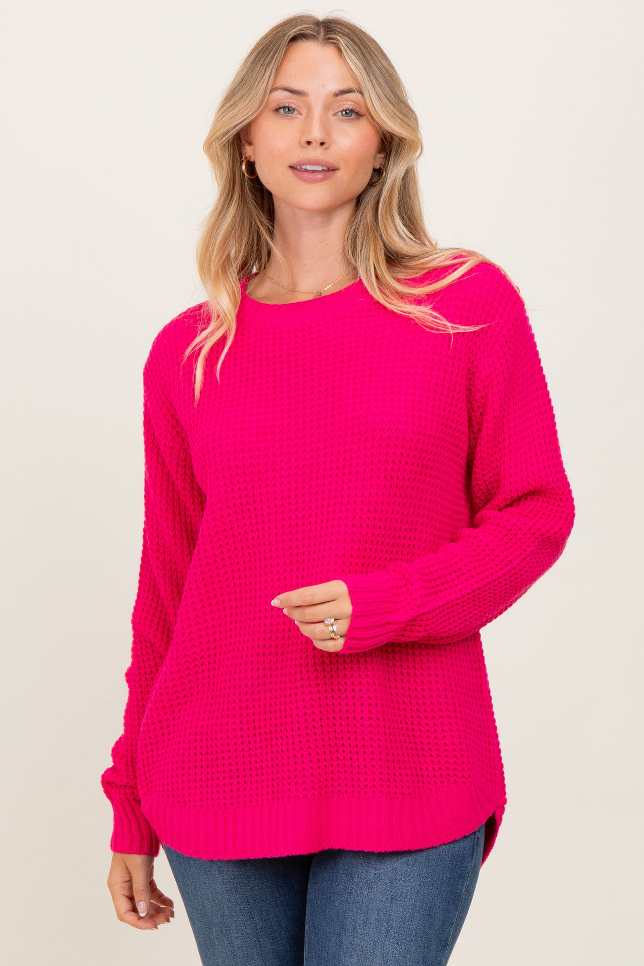woman wearing a bright pink oversized knitted sweater with a round neckline and side slits, paired with blue jeans