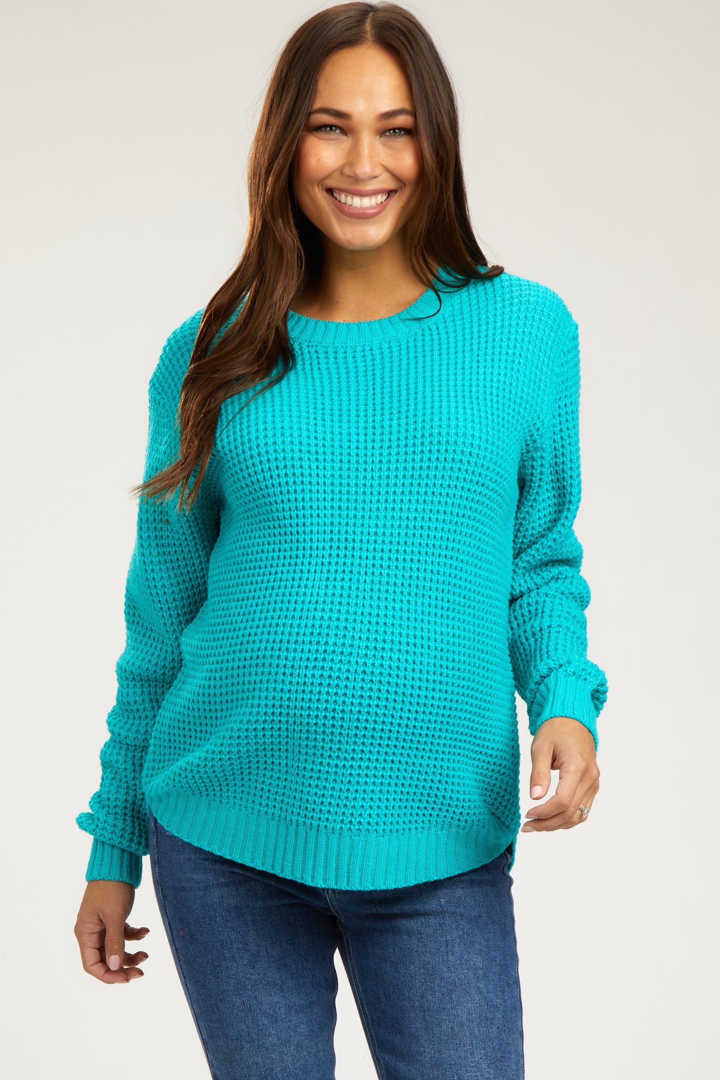 woman wearing a bright turquoise maternity sweater with a loose fit and long sleeves, smiling and showcasing her baby bump