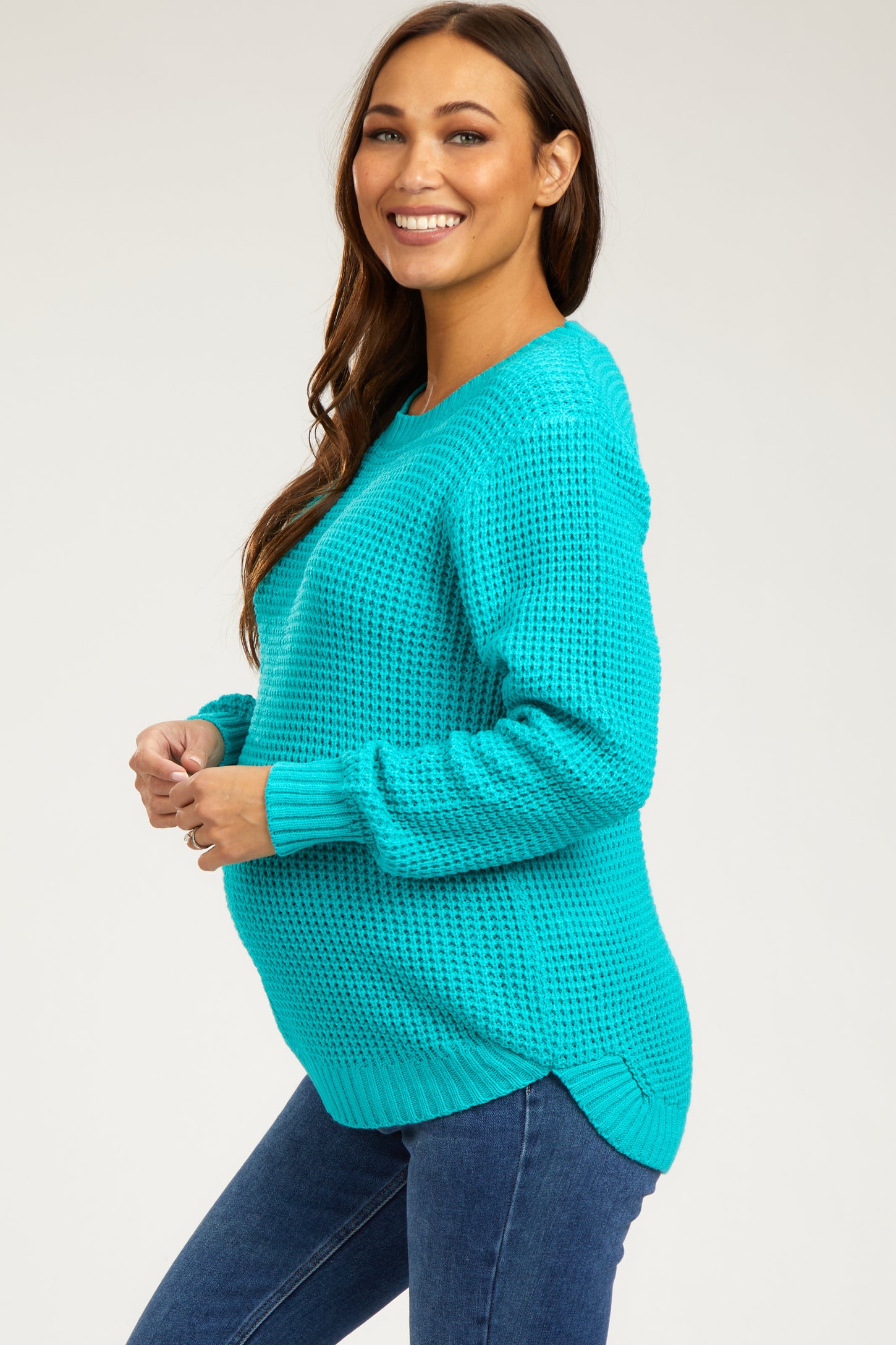 woman wearing a bright teal knit maternity sweater with a visible baby bump, paired with blue jeans
