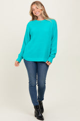 woman wearing a bright turquoise oversized knit sweater and blue skinny jeans, standing with one hand on her hip