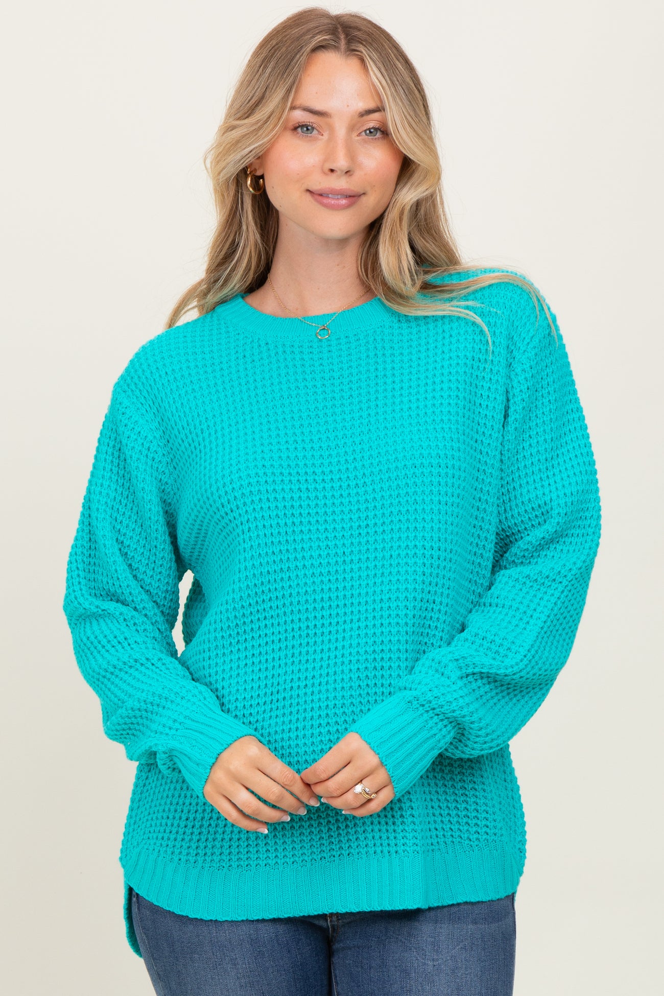 woman wearing a bright turquoise oversized knit sweater with long sleeves and side slits, smiling at the camera