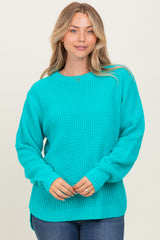woman wearing a bright turquoise oversized knit sweater with long sleeves and side slits, smiling at the camera