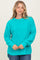 woman wearing a bright turquoise oversized knit sweater with long sleeves and side slits, smiling at the camera