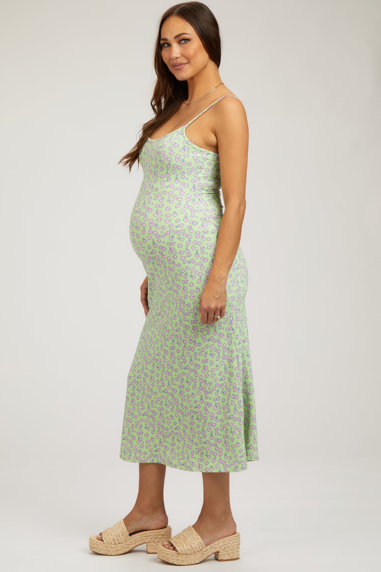 woman wearing a green floral print maternity dress with a fitted silhouette and a visible baby bump