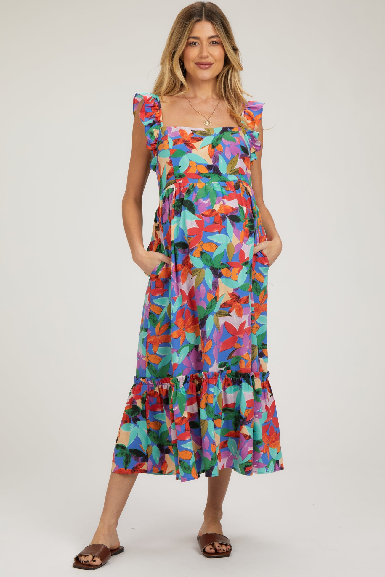 woman wearing a colorful floral maternity dress with ruffle straps and pockets, showcasing her baby bump