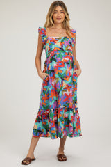 woman wearing a colorful floral maternity dress with ruffle straps and pockets, showcasing her baby bump