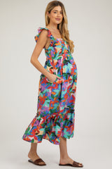woman wearing a colorful floral print maternity dress with ruffled straps and pockets, featuring a visible baby bump