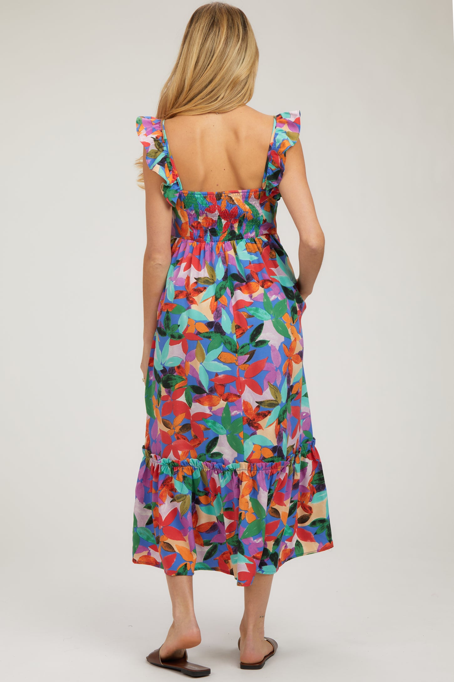 woman wearing a colorful floral print maternity dress with ruffled straps and a tiered hem, showing her back
