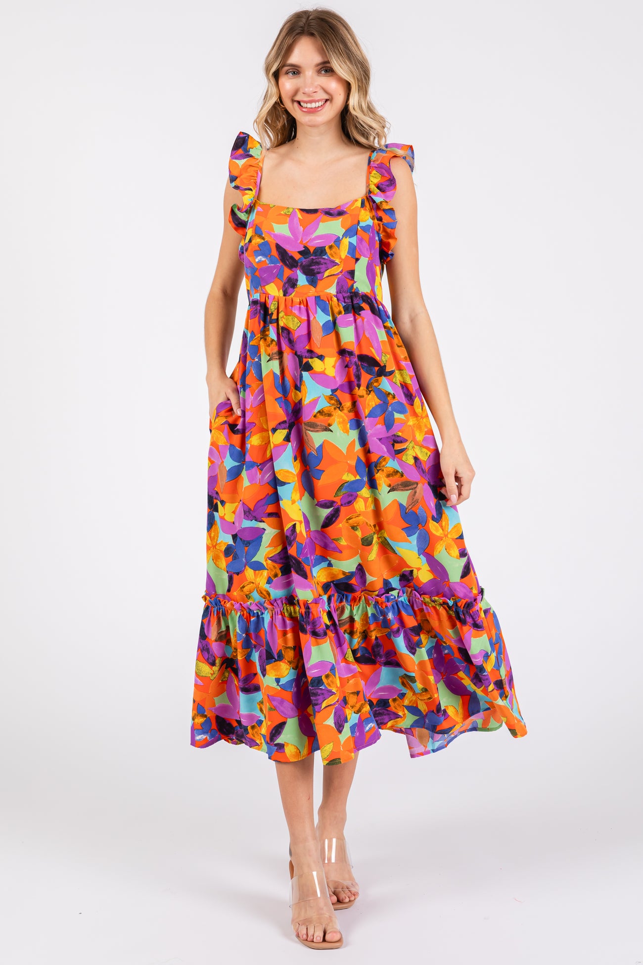 woman wearing a colorful floral midi dress with ruffled straps and pockets, standing against a white background