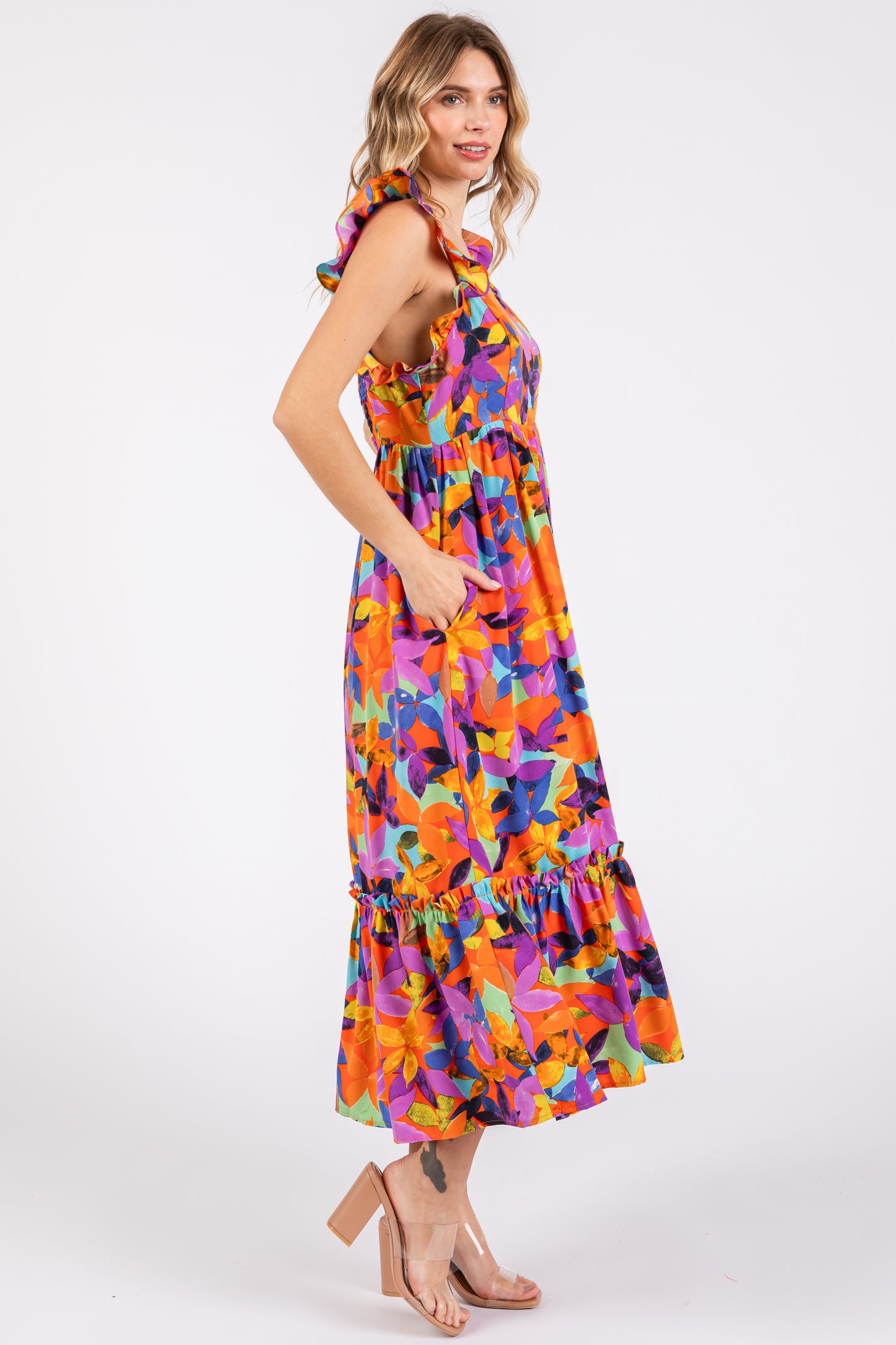 woman wearing a colorful floral maxi dress with ruffle straps and pockets, standing in profile