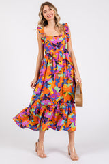 woman wearing a colorful floral midi dress with ruffled straps and a tiered hem, holding a wooden handbag