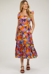 woman wearing a colorful floral maternity dress with ruffled sleeves and a tiered skirt, showing her baby bump