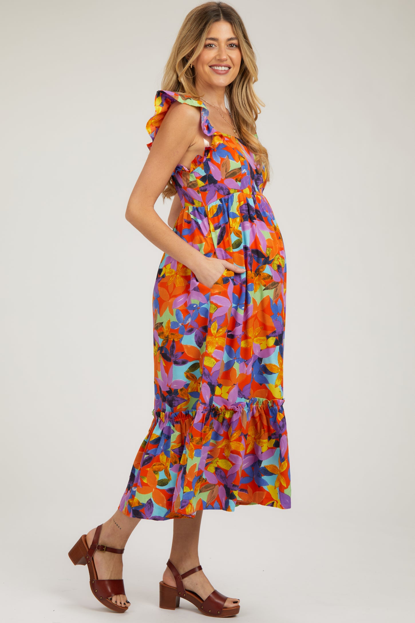 woman wearing a colorful floral maternity dress with ruffles and pockets, and showing a baby bump