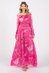 woman wearing a pink off-the-shoulder maxi dress with floral print and smocked waist, standing and smiling
