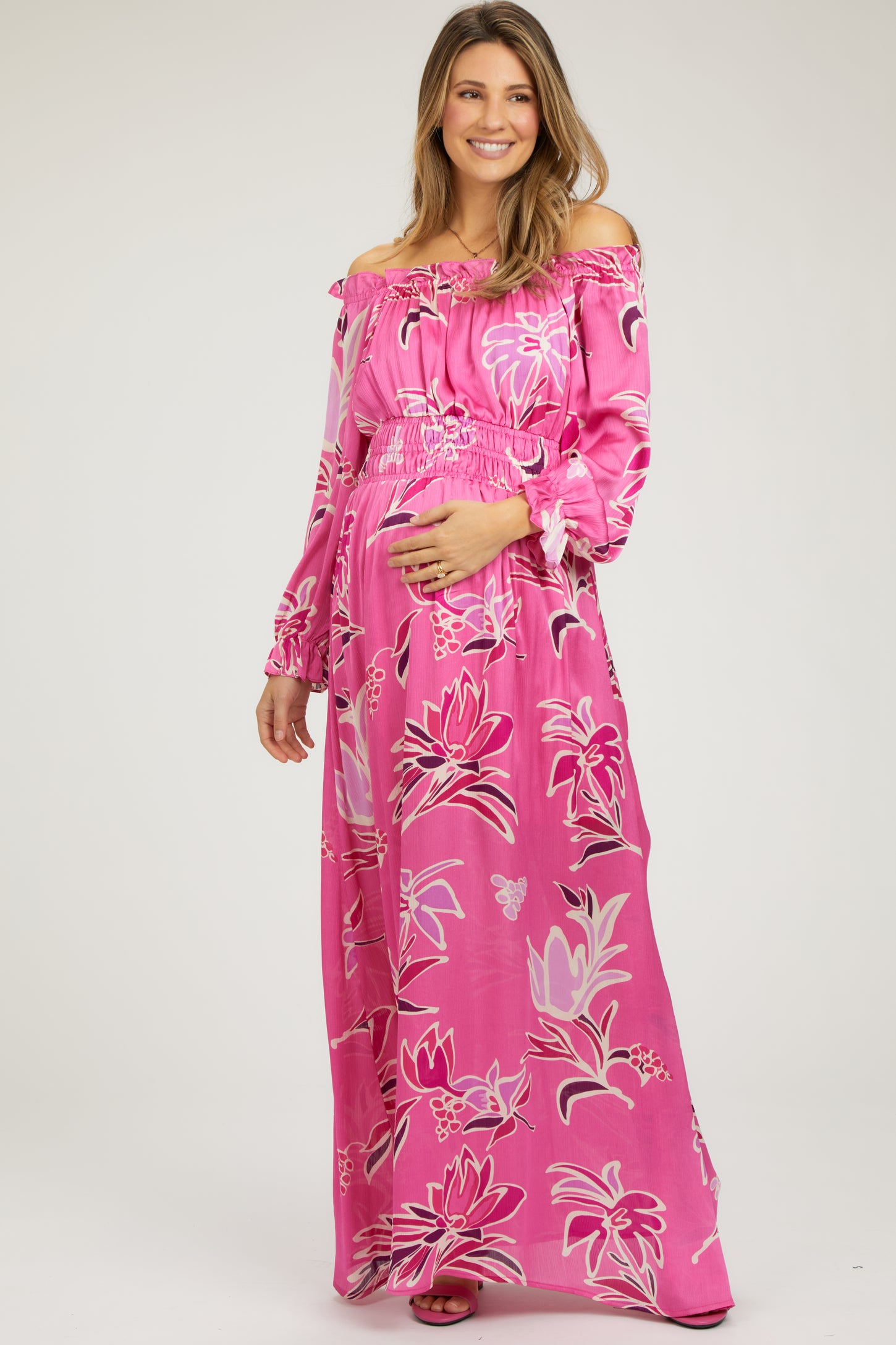 woman wearing a pink floral off-the-shoulder maternity maxi dress and holding her baby bump