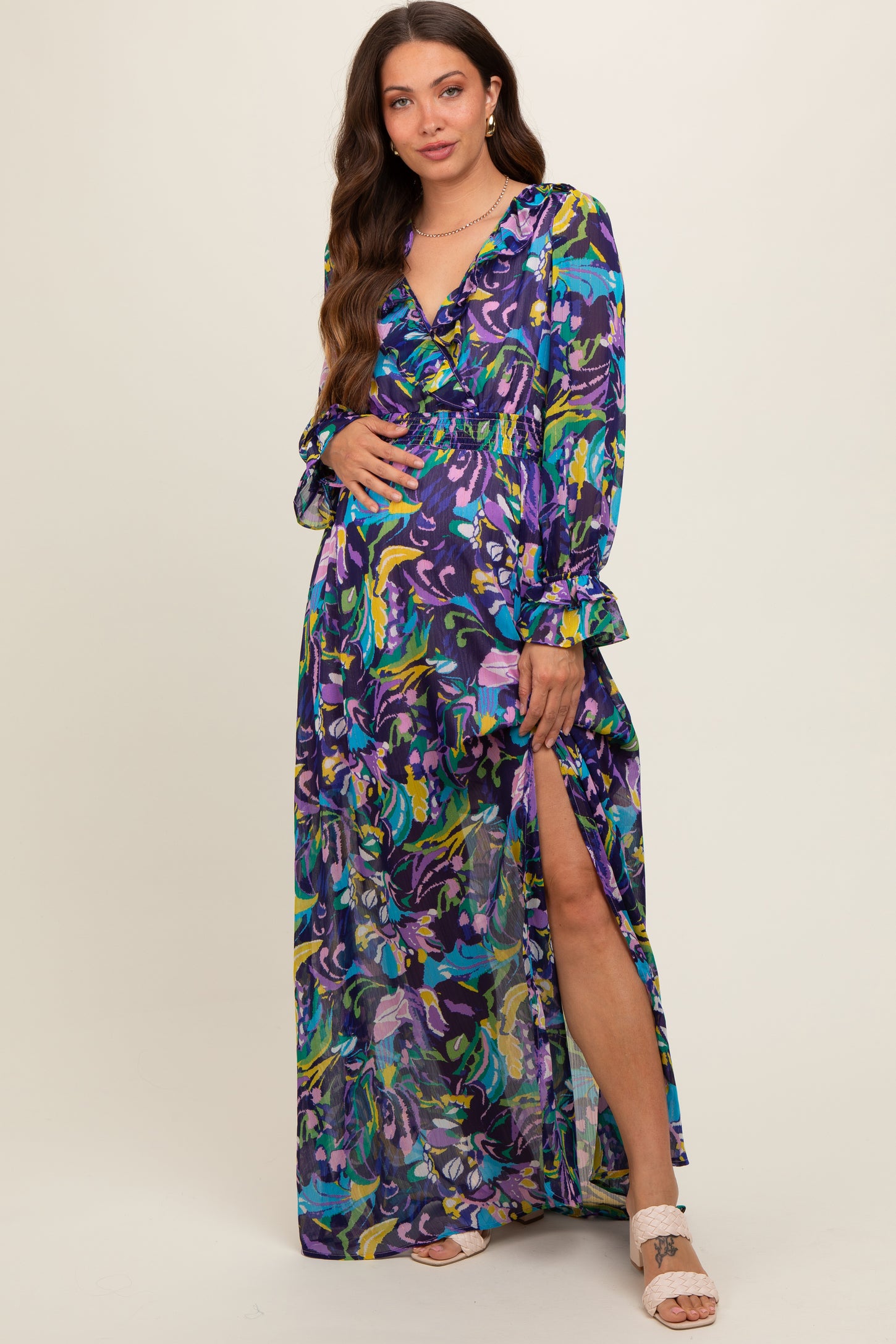 woman wearing a colorful floral print maternity maxi dress with long sleeves and a side slit, showcasing her baby bump