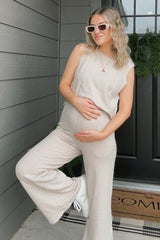 woman wearing a beige sleeveless maternity jumpsuit and holding her baby bump