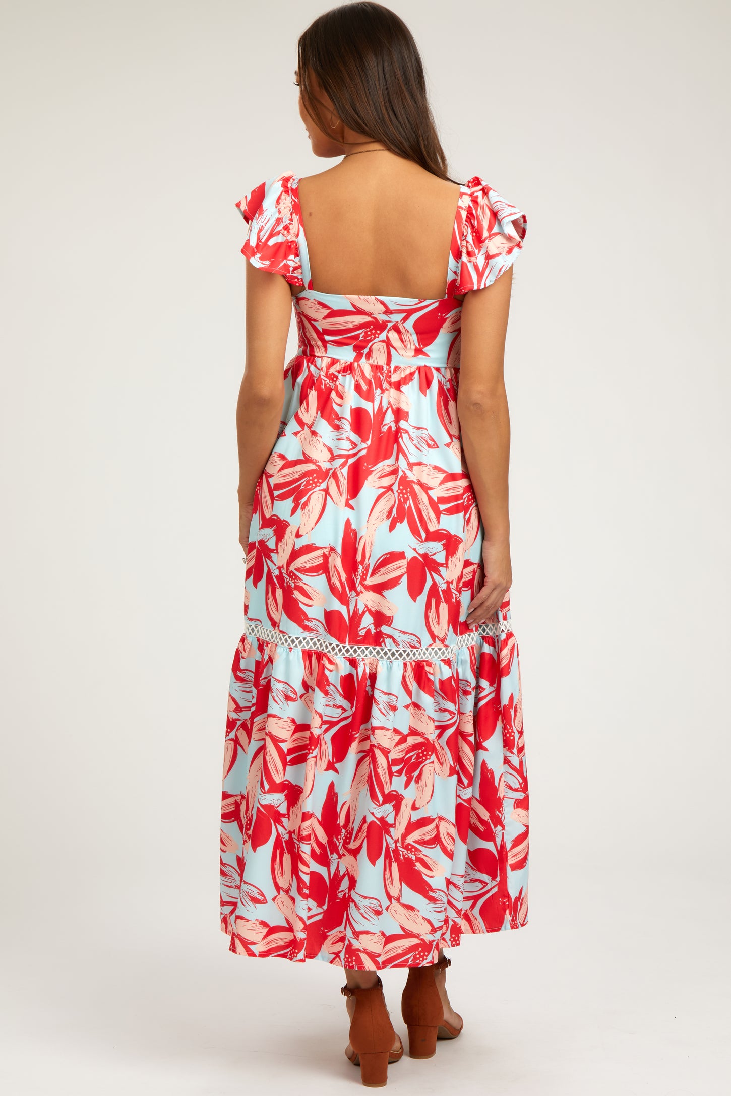 woman wearing a floral maternity maxi dress with ruffled sleeves and a tiered hem, showing her back