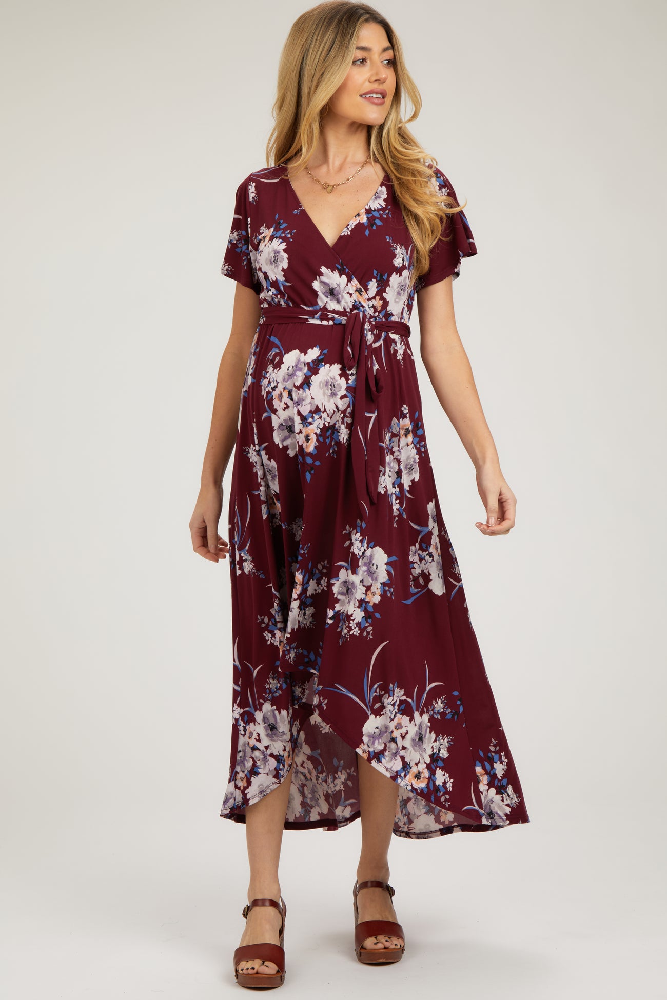 woman wearing a burgundy floral wrap maternity dress with flutter sleeves and a high-low hem, showcasing her baby bump